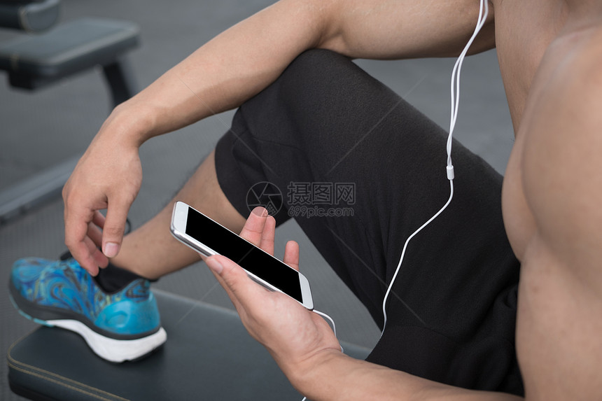 年轻人在健身中心使用手机男运动员在健身房用手机听音乐锻炼后在健身俱乐部休息的图片