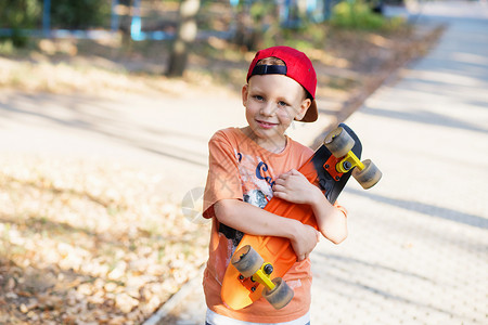 带着便士滑板的城市小男孩子们在夏季公园滑冰城市风格城市孩子孩子背景图片