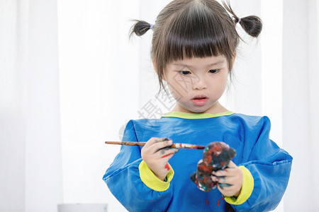 一个可爱的小女孩在乱七八糟地玩颜料的肖像图片