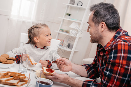 快乐的父亲和女儿在早晨吃果酱烤面包时图片