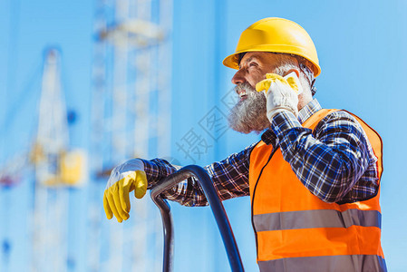 身穿反射背心和硬帽的工人在建筑工地用智能手机交谈图片