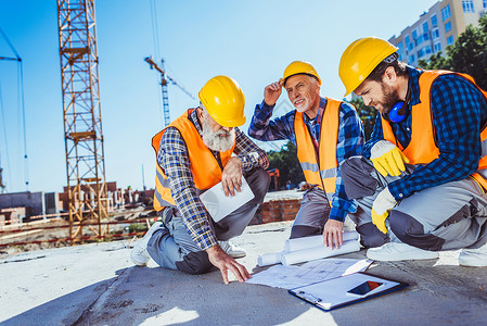 三名身着制服的建筑工人坐在建筑工地混凝土上图片