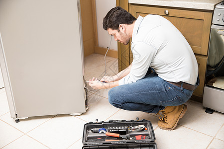 具有吸引力的男电动家在住宅厨房修理冰箱的概图片