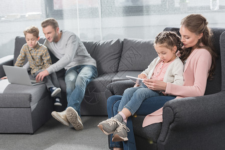 年轻家庭与孩子一起坐在客厅沙发上并使用数字装图片