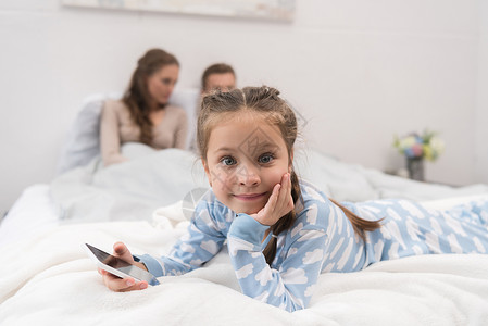 女儿躺在有智能手机的床上父母坐在图片