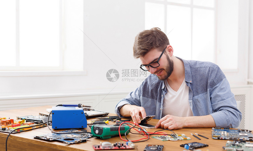 在修理车间拆卸智能手机的男子年轻修理工将移动电话部件分离出来进行诊图片