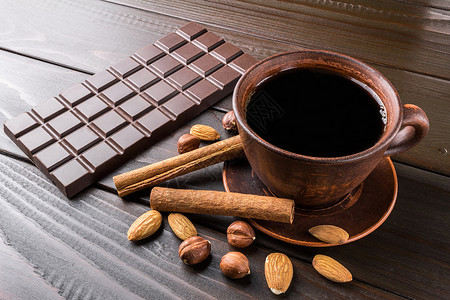 棕色粘土杯中的热黑咖啡深巧克力棒杏仁栗子和木图片