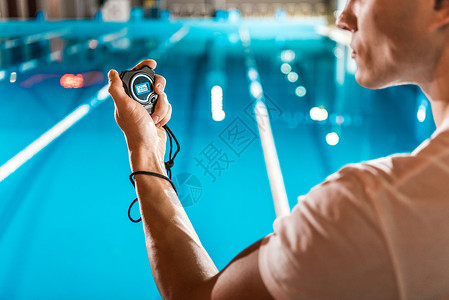 游泳教练用手表站立在比赛游泳池图片