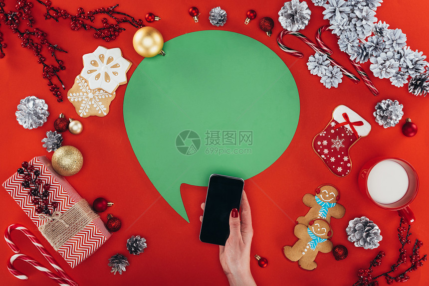用智能手机绿色言语泡沫圣诞节装饰品和姜面包饼干切成的手观光图片