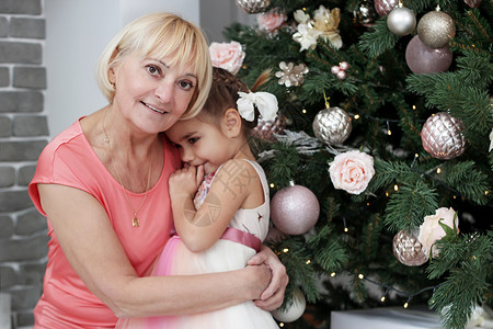 快乐的祖母在圣诞礼物和装饰的树上拥抱孙女的肖像图片