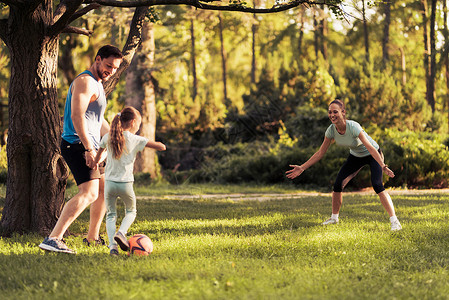 父亲和女儿用红色足球踢足球他们在公园里玩耍扮演图片