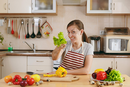 围裙的年轻有魅力的女人有莴苣叶在厨房里节食的概念健康的生活方式在家做图片