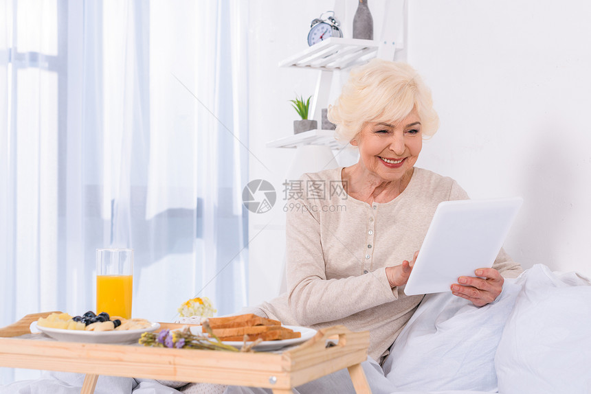 在家用平板电脑在床上吃早餐的图片