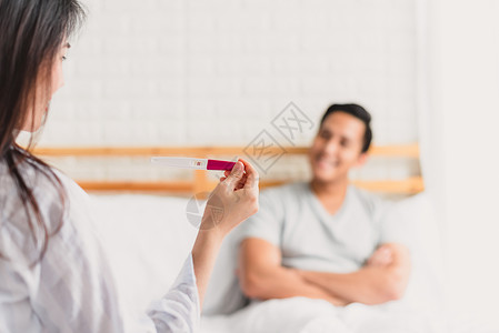 一张快乐的亚洲女人在卧室里显示阳妊娠试验的照片图片