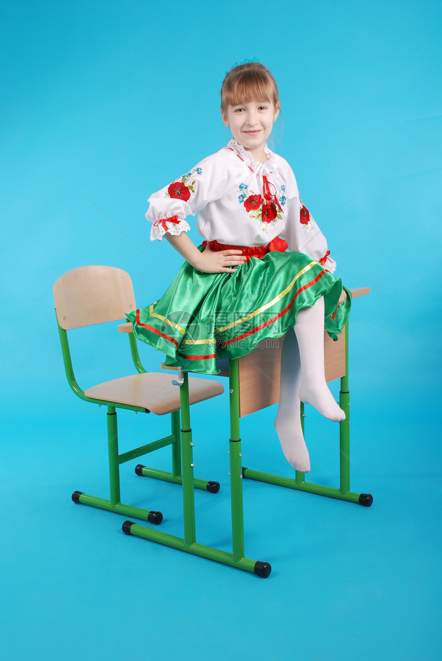 在乌克兰刺绣中有轻头发的年轻女孩坐在书桌上图片