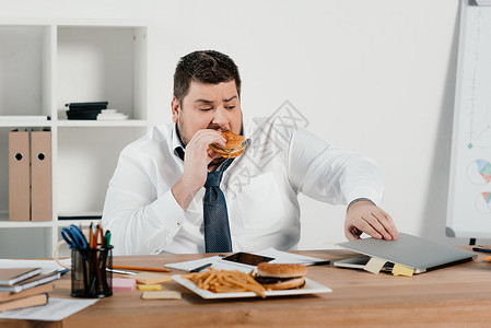 超体重商人吃汉堡包和办公室使图片