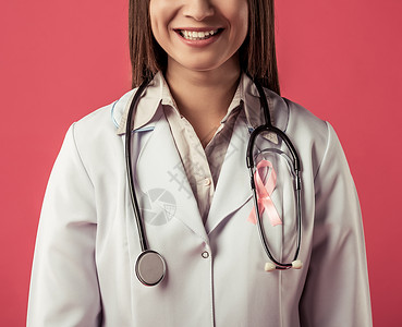 以红色背景微笑的胸前带有粉色丝带的美丽女医生被割成像图片