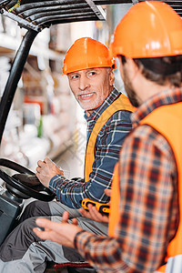 身穿安全背心和安全背心和头盔的高级工人坐在叉车机上图片