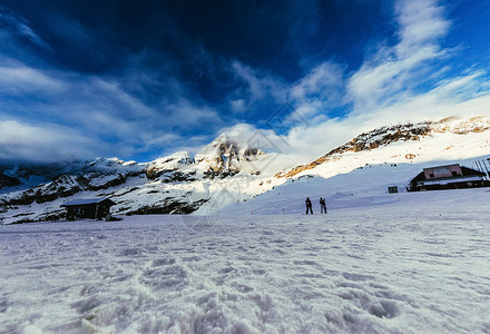 蓝色天空下平静的山脉风景与游客在雪上图片