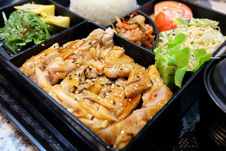 传统日本料理便当盒或多层盒配照烧鸡肉饭沙拉玉子烧或煎蛋卷日式裙带菜或海背景图片