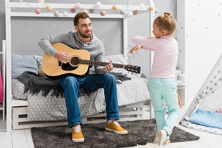 快乐的父亲在卧室为女儿弹吉他当她着女儿图片