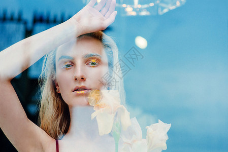 那个年轻金发美女的肖像和时装外星女郎站在玻璃后面的花朵旁边图片