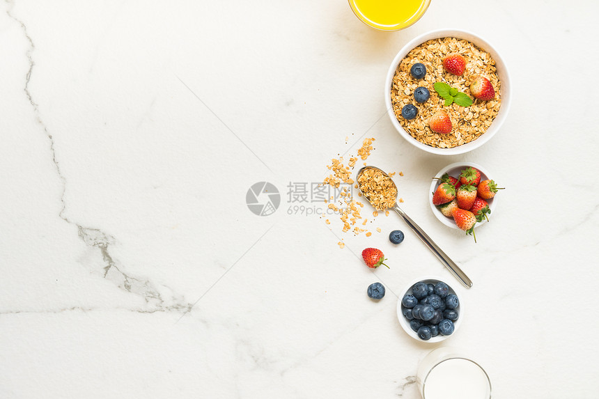 以蓝莓草莓和黑咖啡牛奶及橙汁为白石桌背景的Granola图片