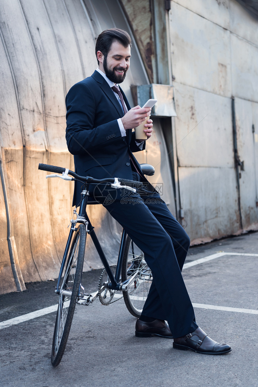 带着咖啡微笑的商人在街上靠着自行车时使用智能图片