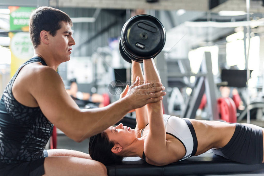 在现代体育馆的轮椅上帮助美貌女举重锻炼运动的人教官肌肉图片