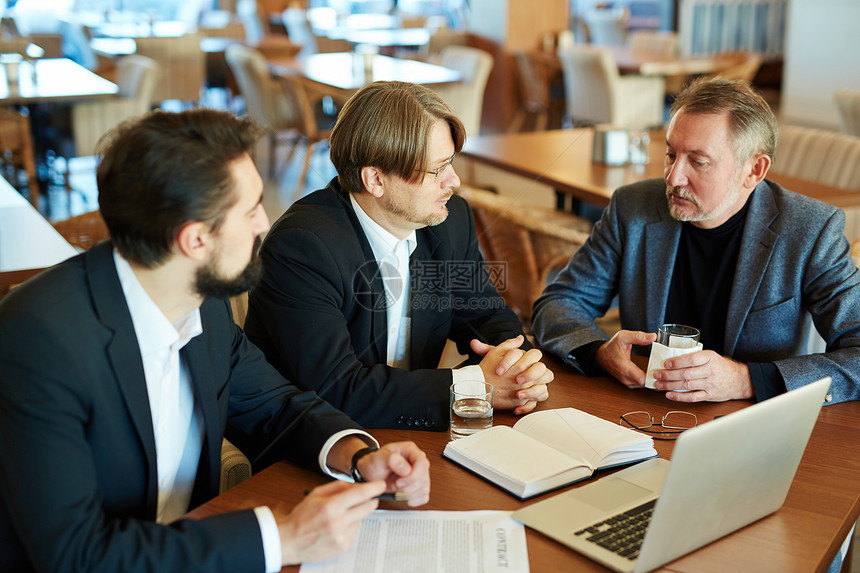三位自信的正装商业伙伴坐在宽敞的餐厅里讨论新的合同条款图片