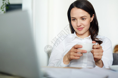 有茶杯的女商人在网上观看视频或通过视频图片