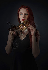 穿着黑色裙子的美丽的红头发女人戴着嘉年华面具金色狂欢节面具图片