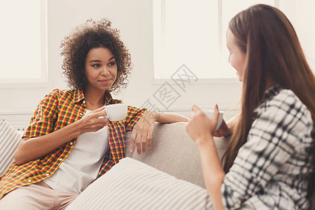 闲话半盏茶两个快乐的年轻女朋友拿着咖啡杯在家里的客厅里聊天背景