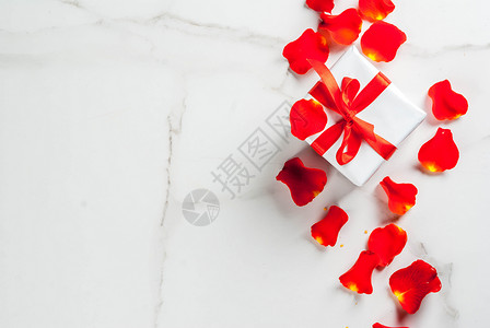 玫瑰花瓣和带红丝带的白色包装礼盒图片