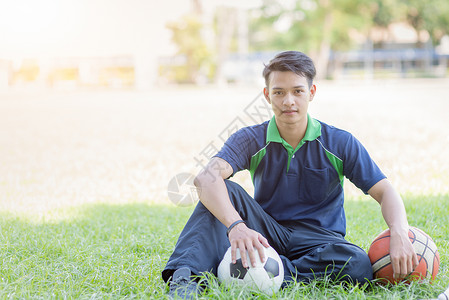 聪明男孩坐在足球和篮球的绿草体育和健康概念上坐以图片