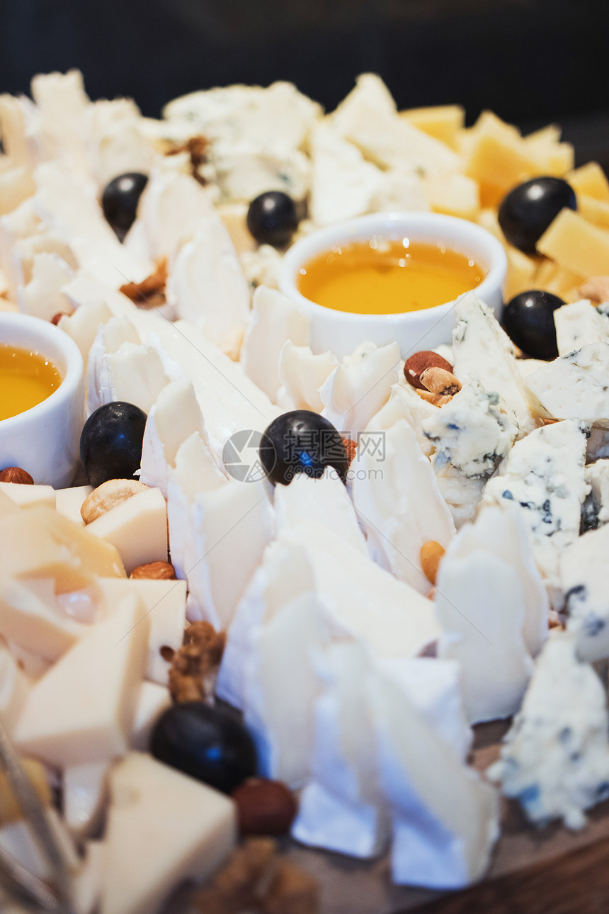 奶酪盘在白色混凝土纹理背景上的白色木服务板上用蜂蜜杓子制作的各种奶酪核桃和蜂蜜带空间的顶视图图片
