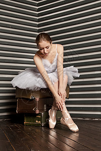 她是一个可爱的年轻芭蕾舞女郎穿着白色古典礼服坐在一堆黑白背景的图片
