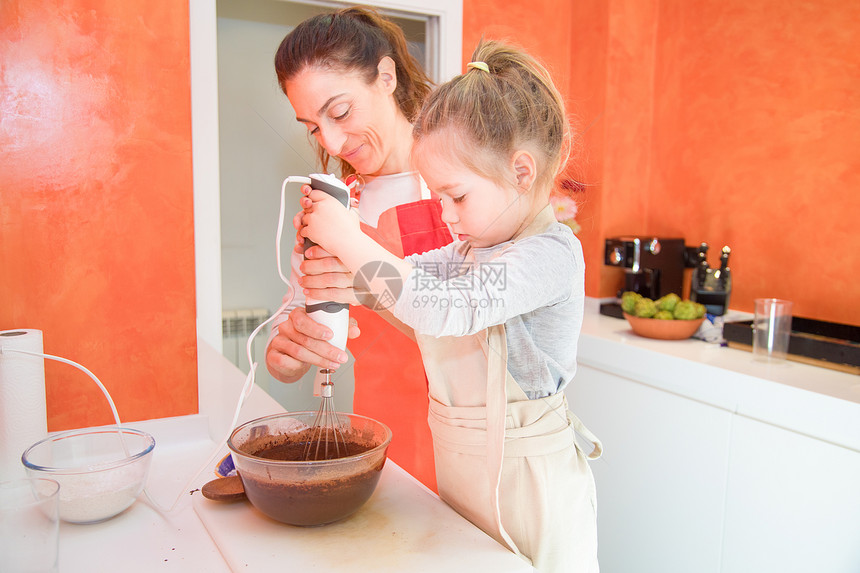 四岁的孩子用搅拌机或电动搅拌机在玻璃碗里打巧克力奶油图片