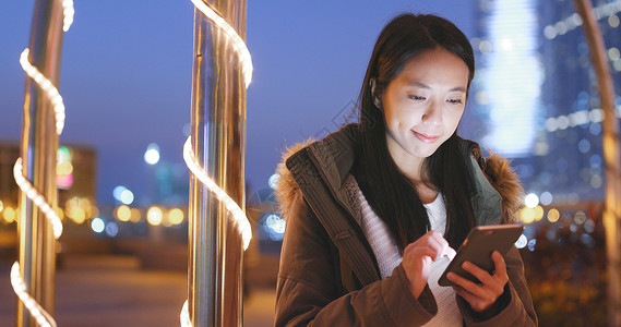 夜间在城市使用智能手机的年轻女图片