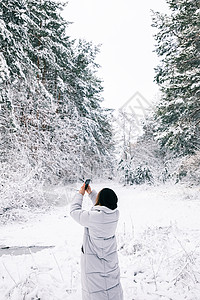 妇女用智能手机拍摄雪林照图片