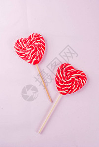 情人节的日光粉色背景贺卡概念两个红心棒糖或棍棒上的糖果图片