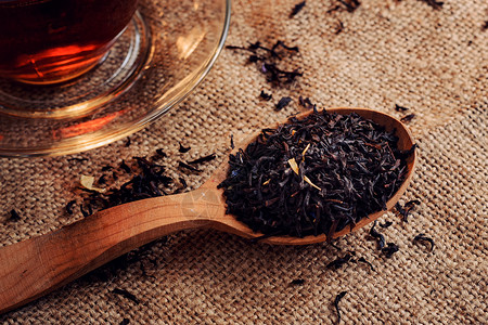 黑茶叶在木制勺子里和一杯熟茶在图片