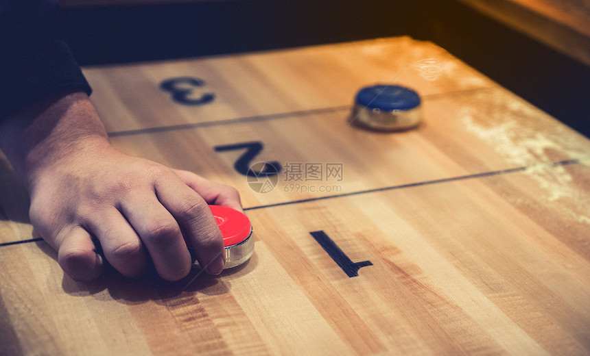 老式洗牌棋盘游戏与红色和蓝色圆盘和手拿着红色蓝圆盘在木制洗牌桌上具有选择焦点的图片