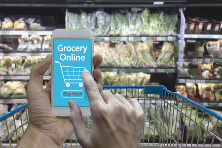 手动使用智能手机与杂货在线屏幕上模糊超市和零售店在购物图片