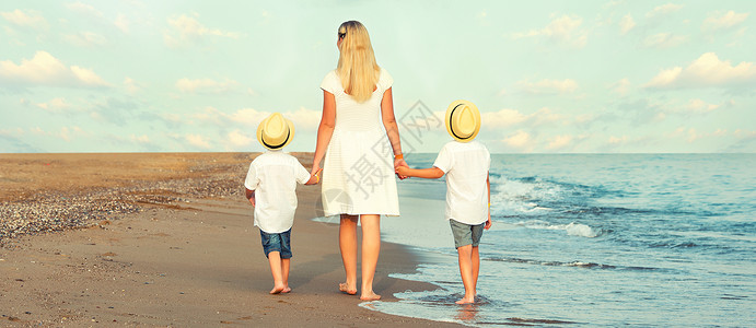 日落时家人在黄昏的沙滩上散步母图片
