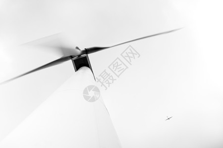 从下方看飞机高空飞行的大型电动环保风力涡轮机图片
