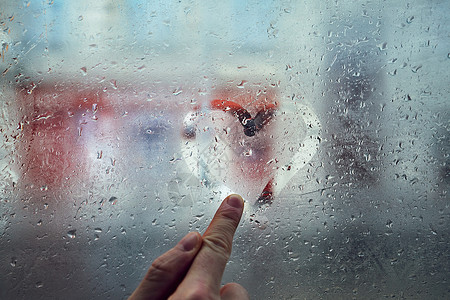 年轻男子的手指在窗户上画出心形与雨滴图片