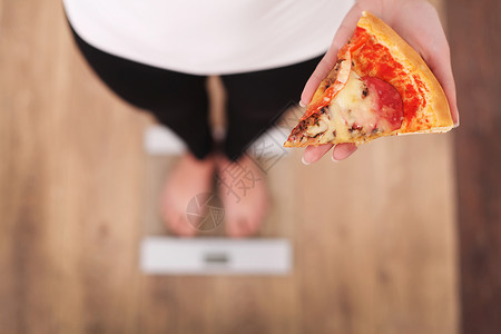 饮食女人在拿着甜圈的体重秤上测量体重糖果是不健康的垃圾食品节食图片