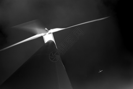 从下方看大型电动环保风力涡轮机对抗黑色天空和白色电动飞机背景图片