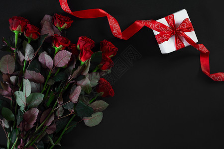 黑色背景的红玫瑰戒指和礼物盒图片